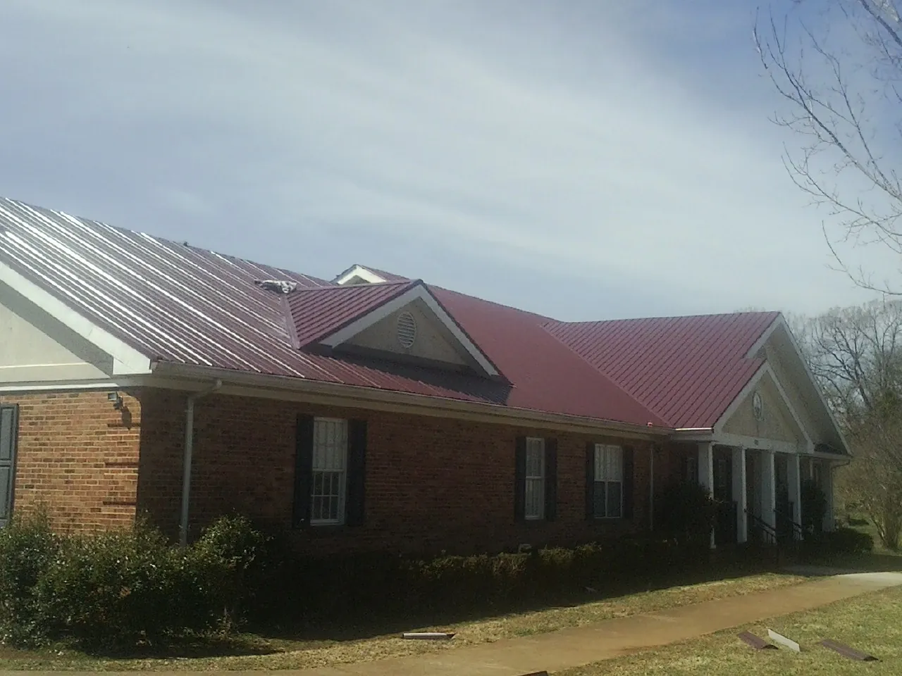 Red metal roof with gabled entries on a long brick building, from a Hail Damage Roof Repair job in Claypool