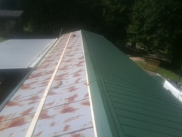 Old rusted panels beside newly installed green metal roofing — Wind Damage Roof Repair by Roofing Brothers in Claypool