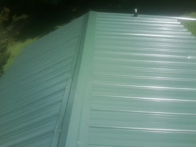 New green metal panels meeting at the ridge of a roof — Flat Roof Repair work by our crew in Claypool