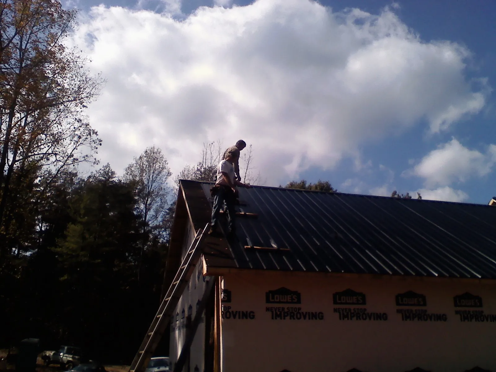 Roofer fastening dark metal panels high against a cloudy sky, from a Roof Inspection job in Claypool