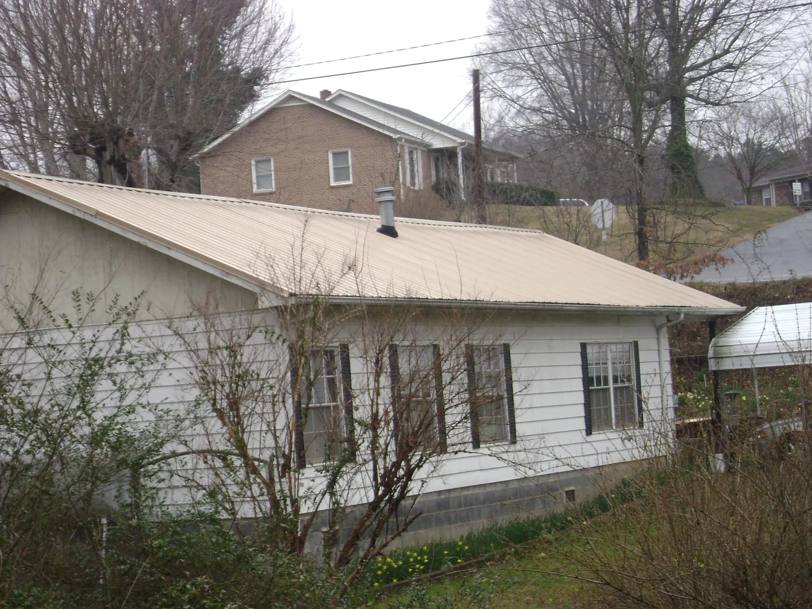 Tan metal roof on a white sided house set into a hillside — Commercial Roofing by Roofing Brothers in Claypool